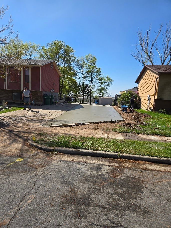 A worker stands on a residential property where a section of a new concrete driveway has been poured.