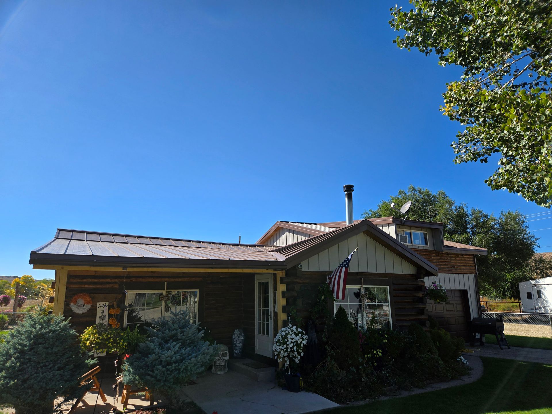 A log cabin house with a metal roof, a front porch with landscaping, and an American flag hanging by the front door.