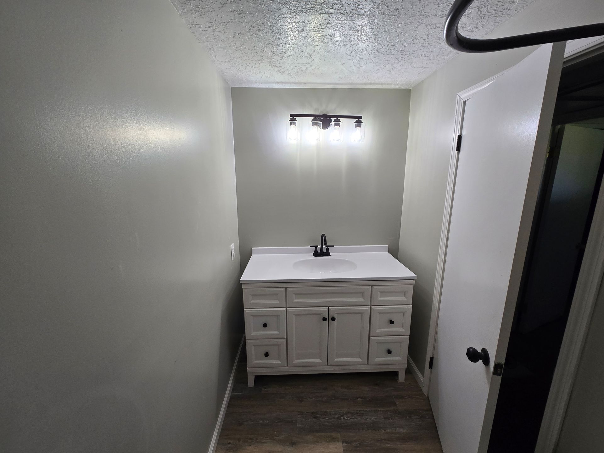 A bathroom vanity with a white cabinet, countertop, and sink, centered on a wall under a modern light fixture.