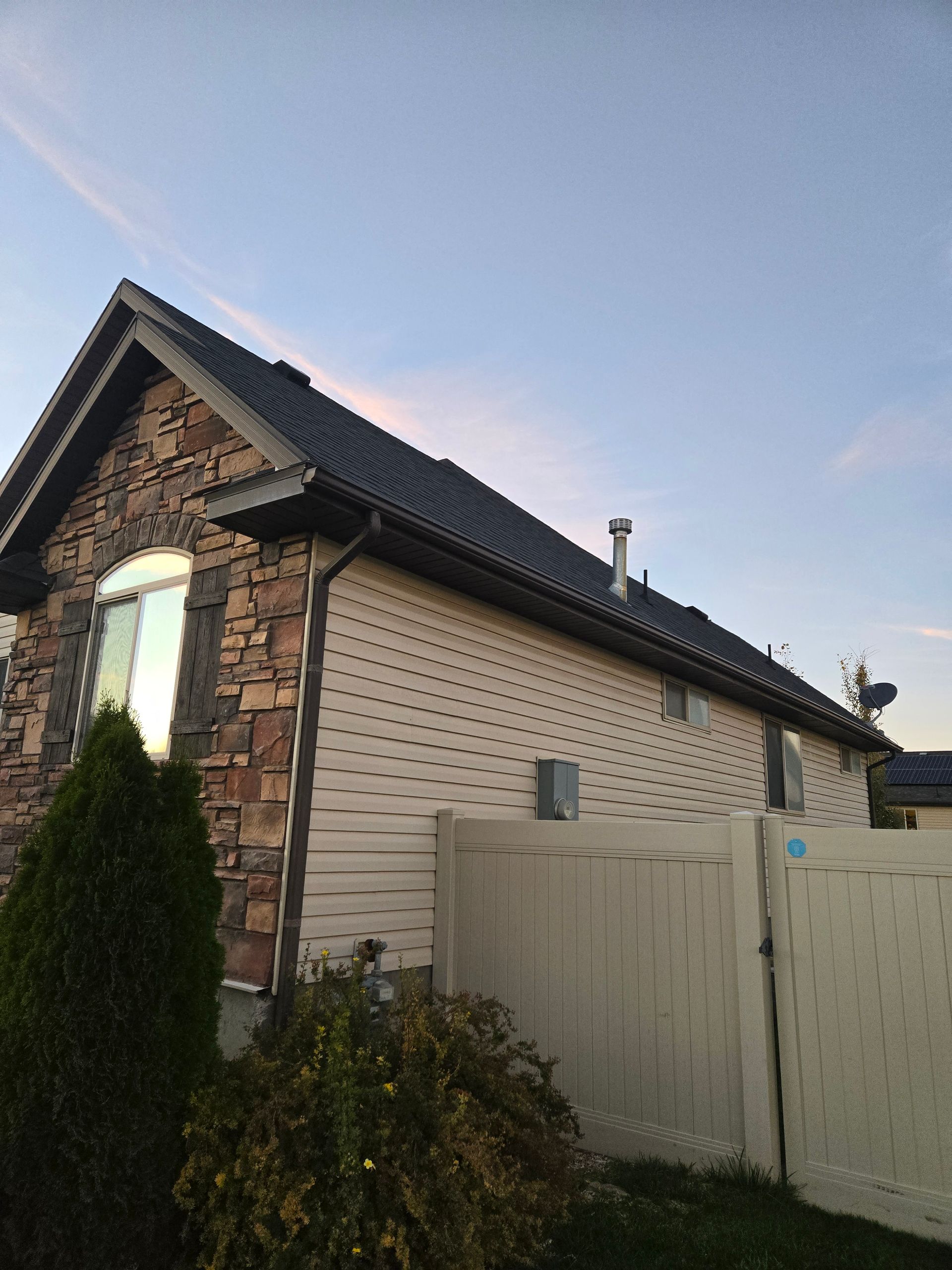 Side view of a house with stone siding on the front, light-colored vinyl siding on the side, and a gray shingled roof.
