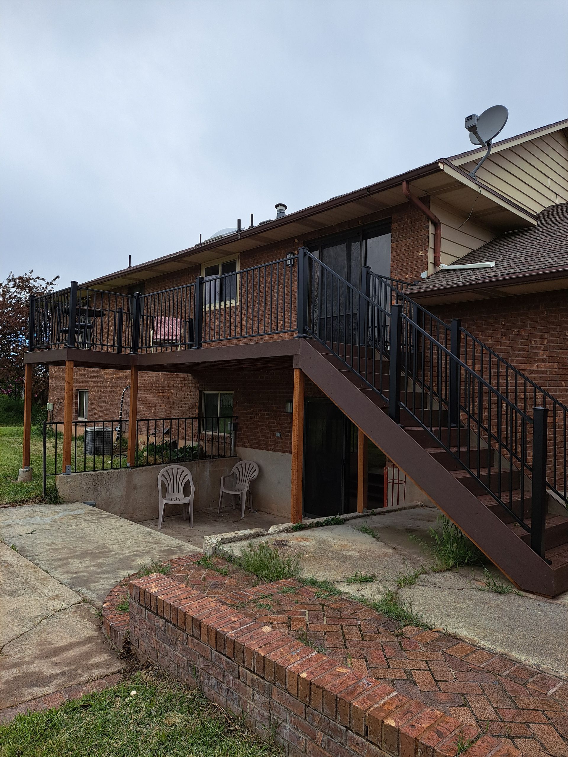 A red brick house exterior features a raised wooden deck with black railings, accessible by a matching metal staircase.