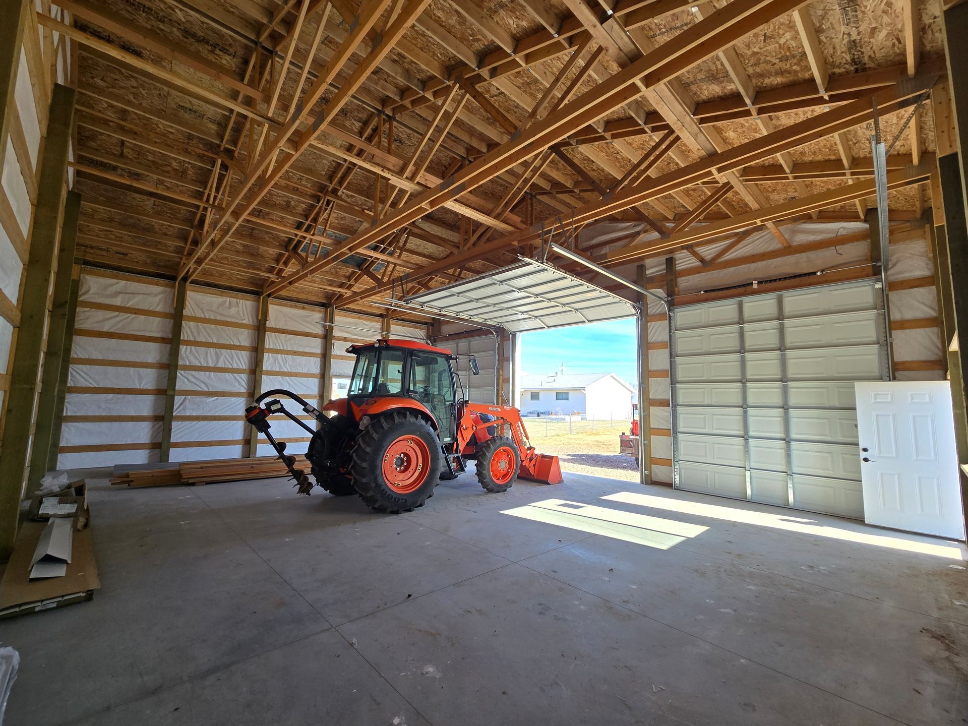 An orange tractor parked inside a large, open-walled metal barn with concrete floors and a partially raised garage door.