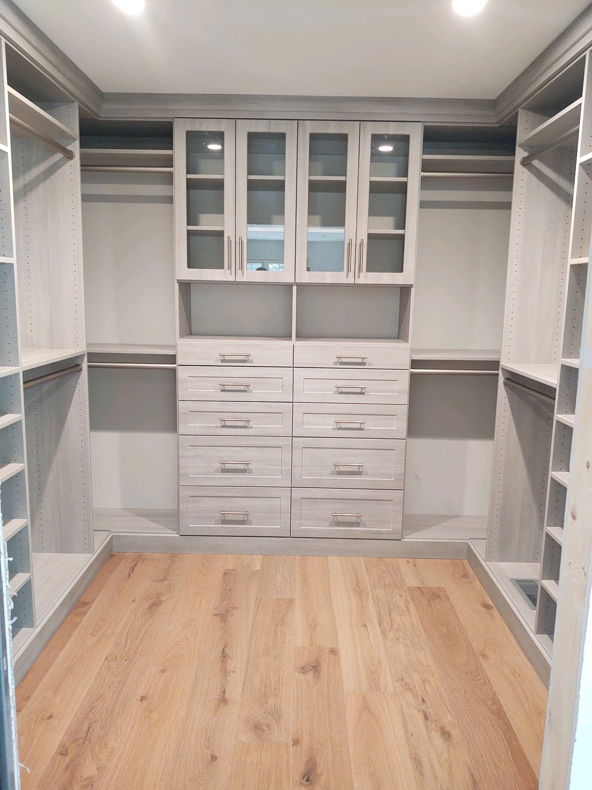 Walk-in closet with light wood-look floor, gray drawers, shelves, and cabinets.