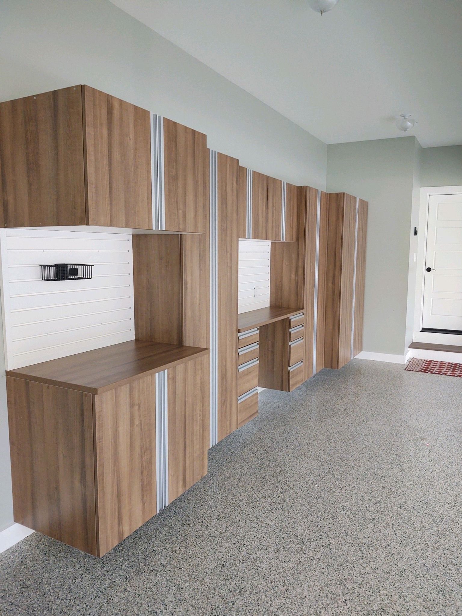 Garage storage cabinets with wood grain finish, gray and white speckled floor, and a neutral wall.