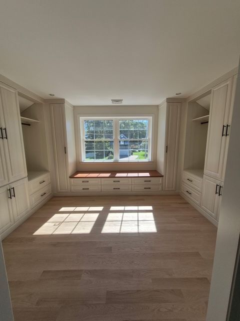A walk-in closet with built-in cabinetry, window seat, and wood floors.