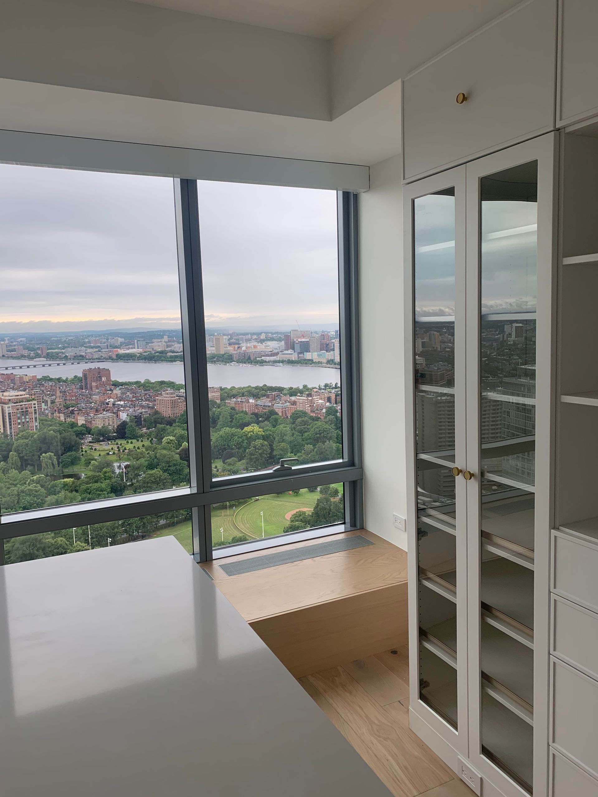 Bright room with large window overlooking a city and a water body, closet with mirrored doors on the right.