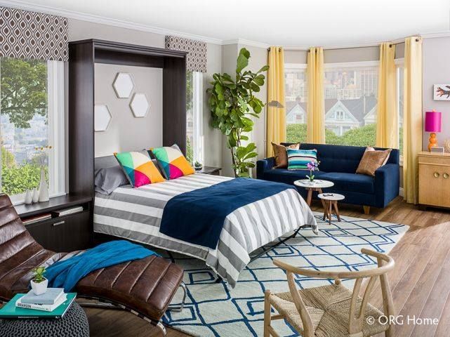 Murphy bed in a living room with blue sofa, yellow curtains, and geometric rug.