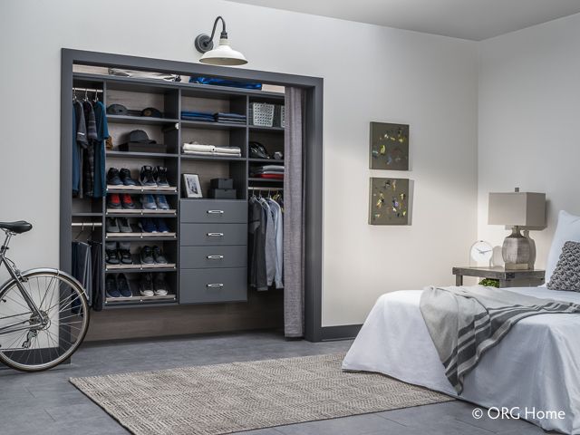 Modern bedroom with open closet; gray shelves, drawers, hanging clothes; bicycle on the left, bed on the right.