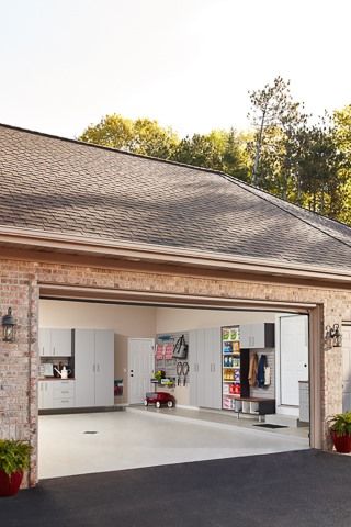 Open garage with organized storage cabinets and accessories inside, brick exterior, asphalt driveway.