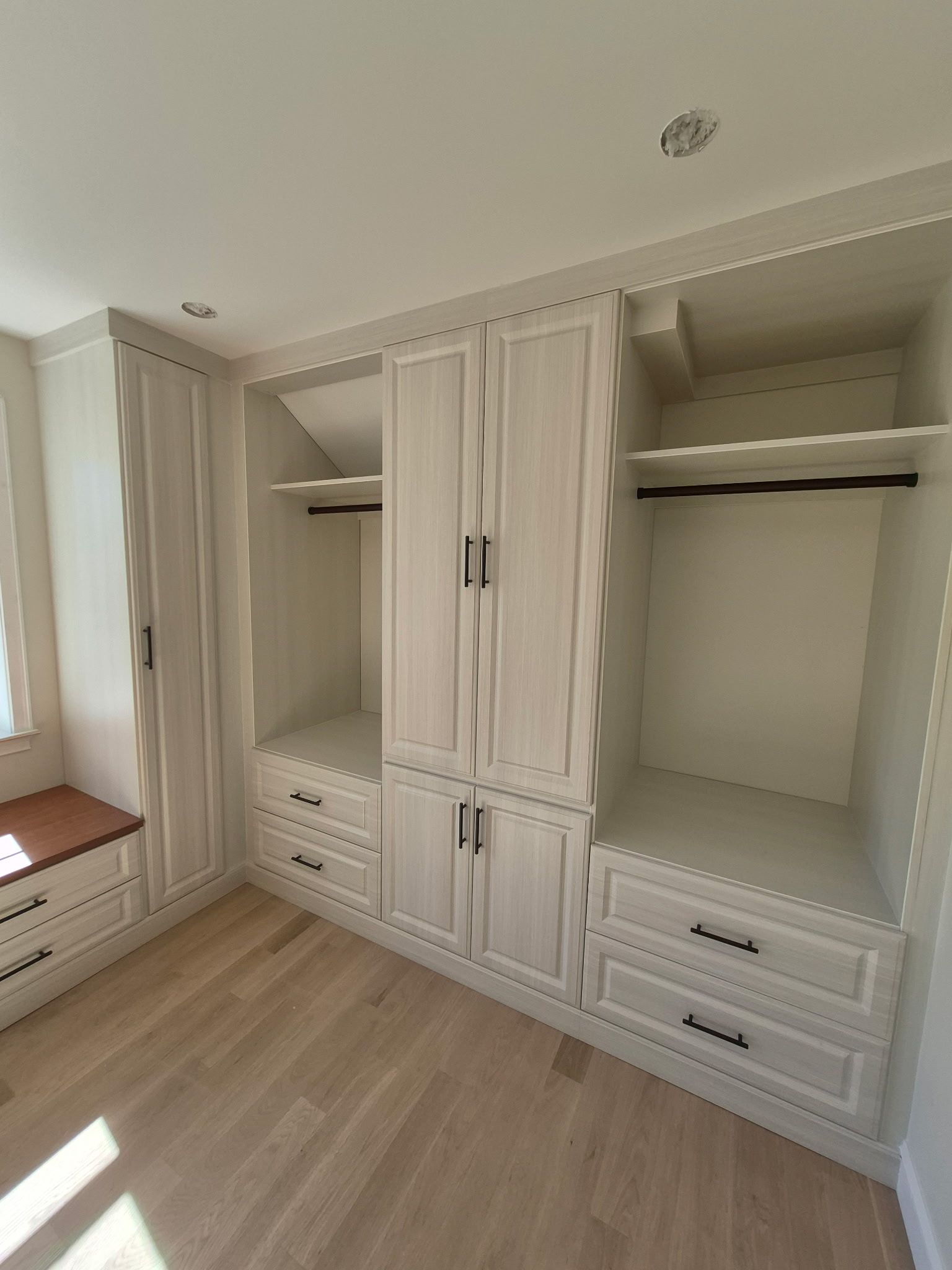 Built-in white wooden closet with drawers, hanging rods, and cabinet doors in a light-floored room.