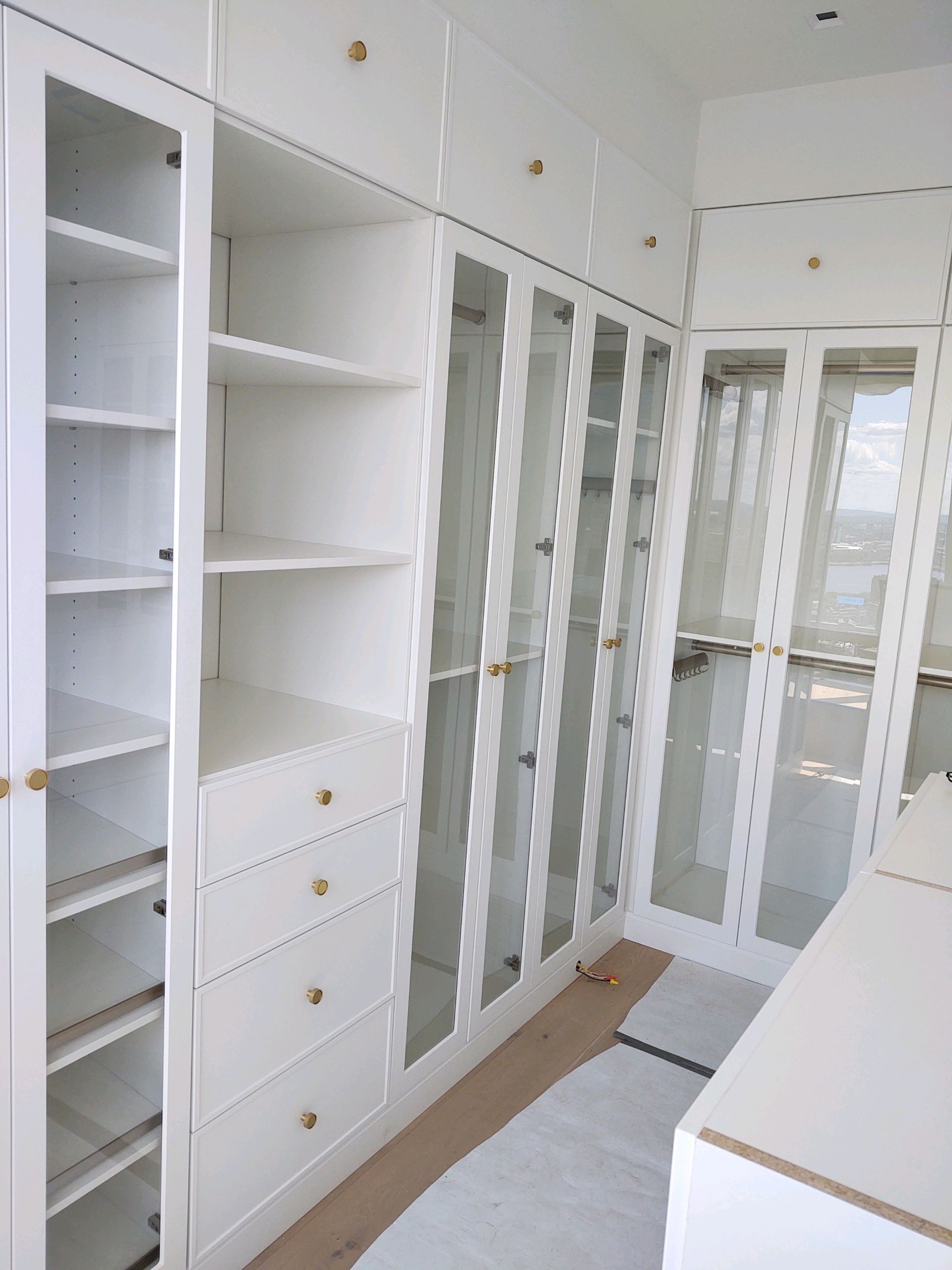 White custom closet with glass doors, shelves, and drawers, brass knobs.