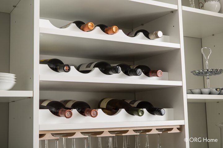 White wine rack holding bottles, with a glass rack below, inside a white cabinet.