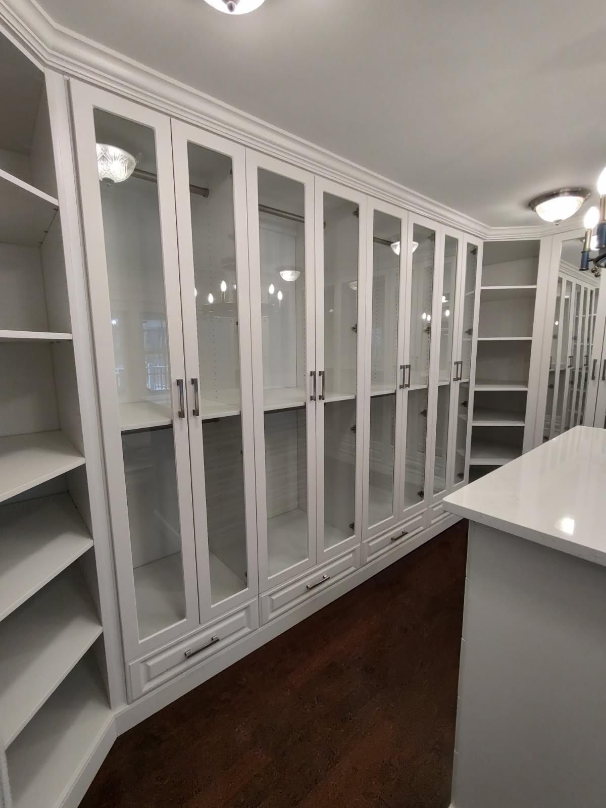 White custom closet with glass-fronted cabinets and open shelves; brown floor; white countertop.