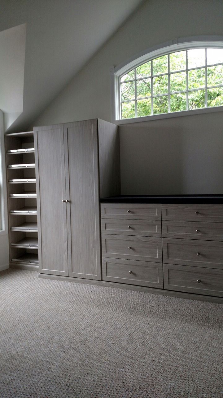 Bedroom with built-in wooden closet, drawers, and shelving; arched window in the background.