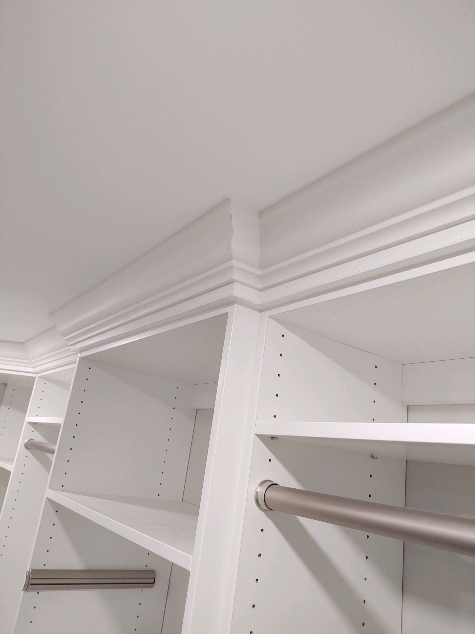 White closet shelving with crown molding against a white ceiling.