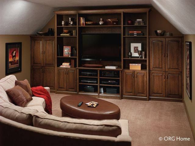 Home theater with brown built-in cabinets, large TV, beige sofa, and ottoman in a room with a sloped ceiling.