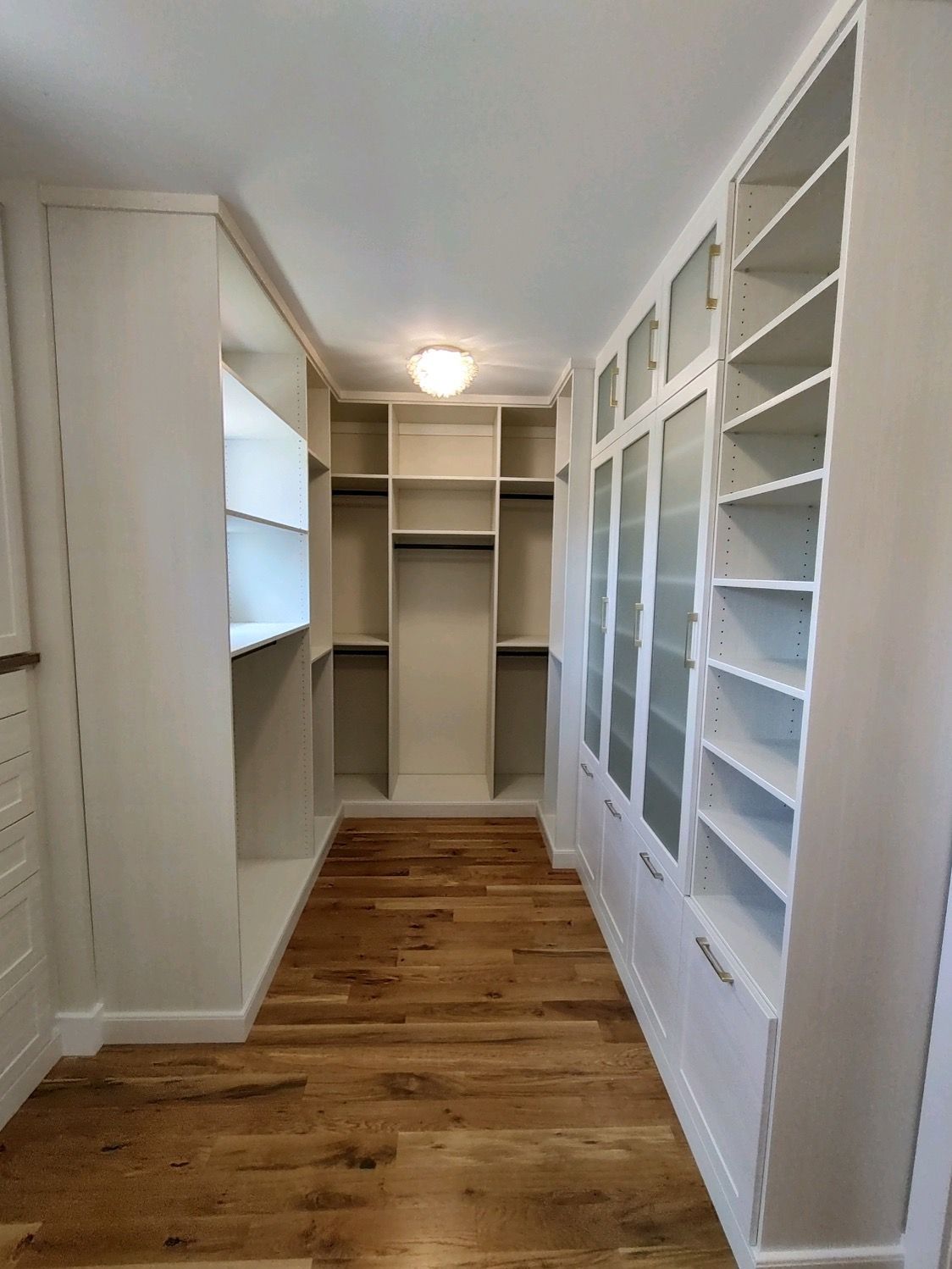 Walk-in closet with white shelves and cabinetry; hardwood floor; glass-paneled doors; neutral light.
