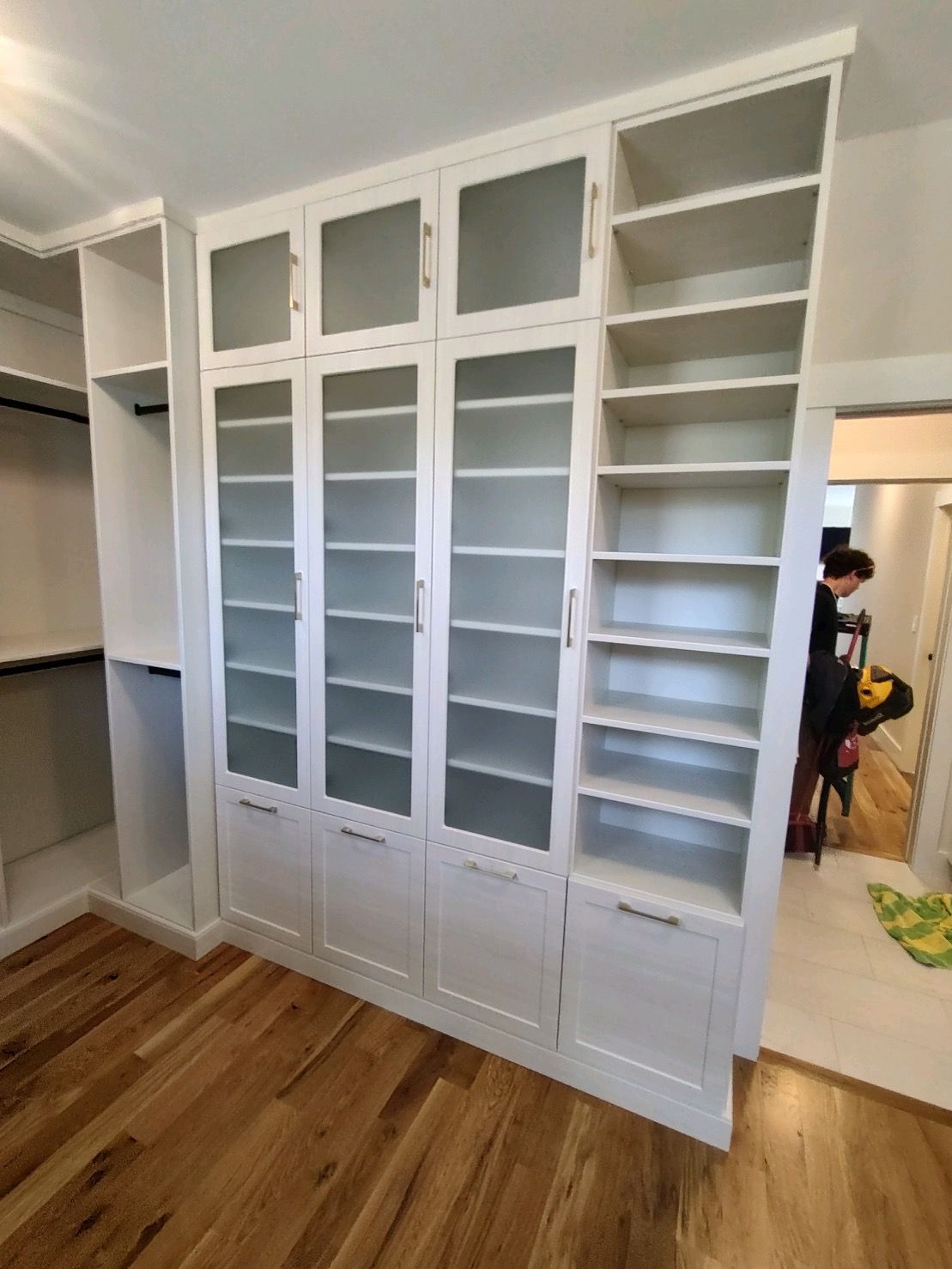 White built-in cabinets with glass doors and open shelving in a room with wood floors.