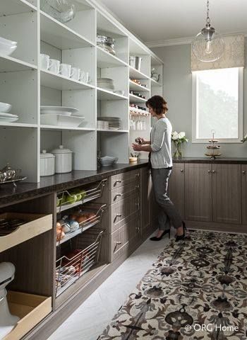 Woman in a pantry, reaching for items. White shelving, gray cabinets, floral rug.