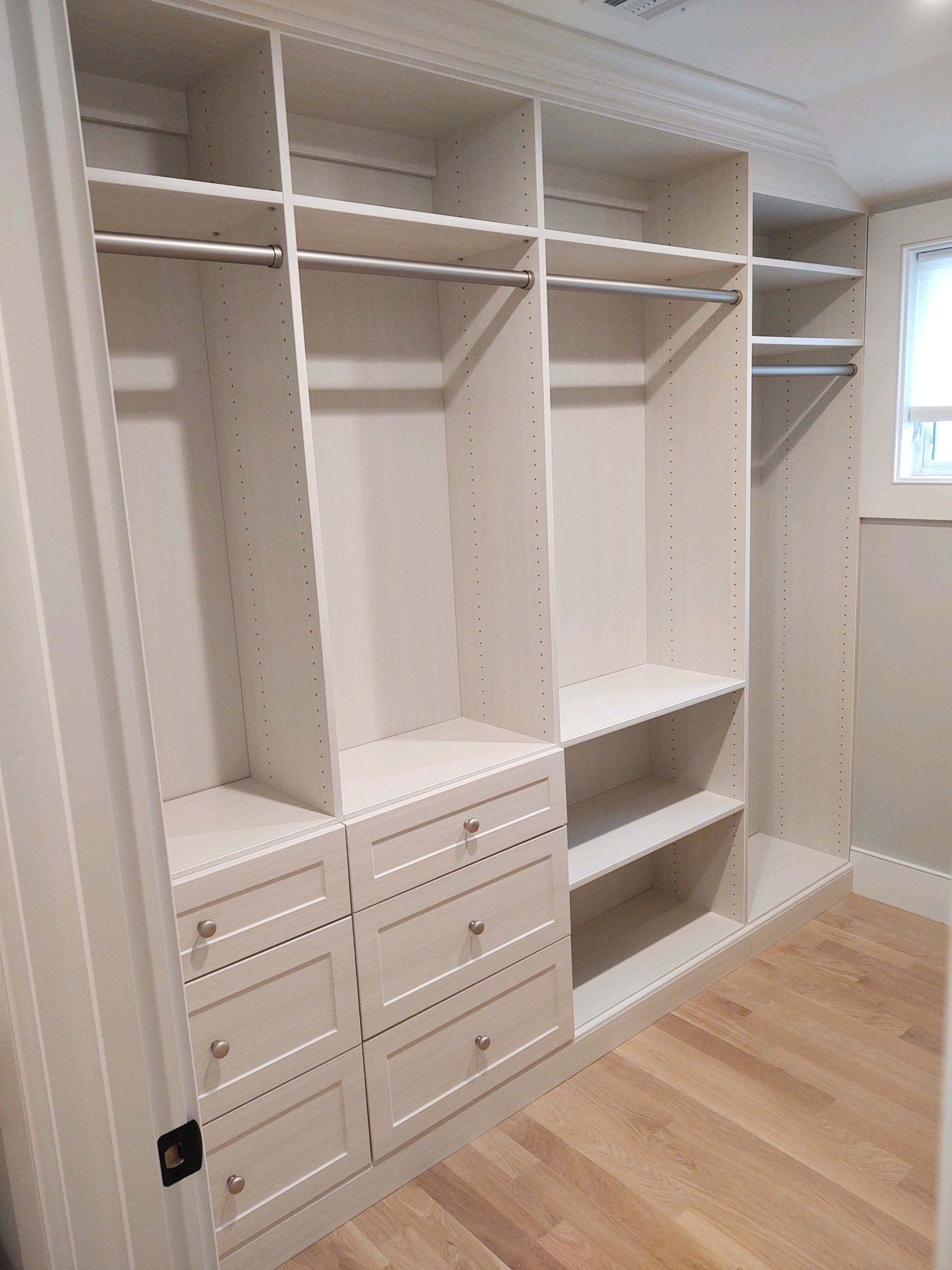 White custom closet with drawers, shelves, and hanging rods. Hardwood floor.