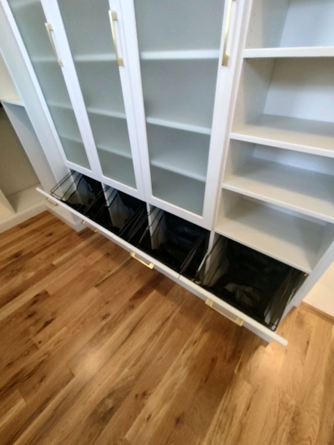 White built-in cabinet with glass doors and open shelves, gold hardware, sitting on wood floor.