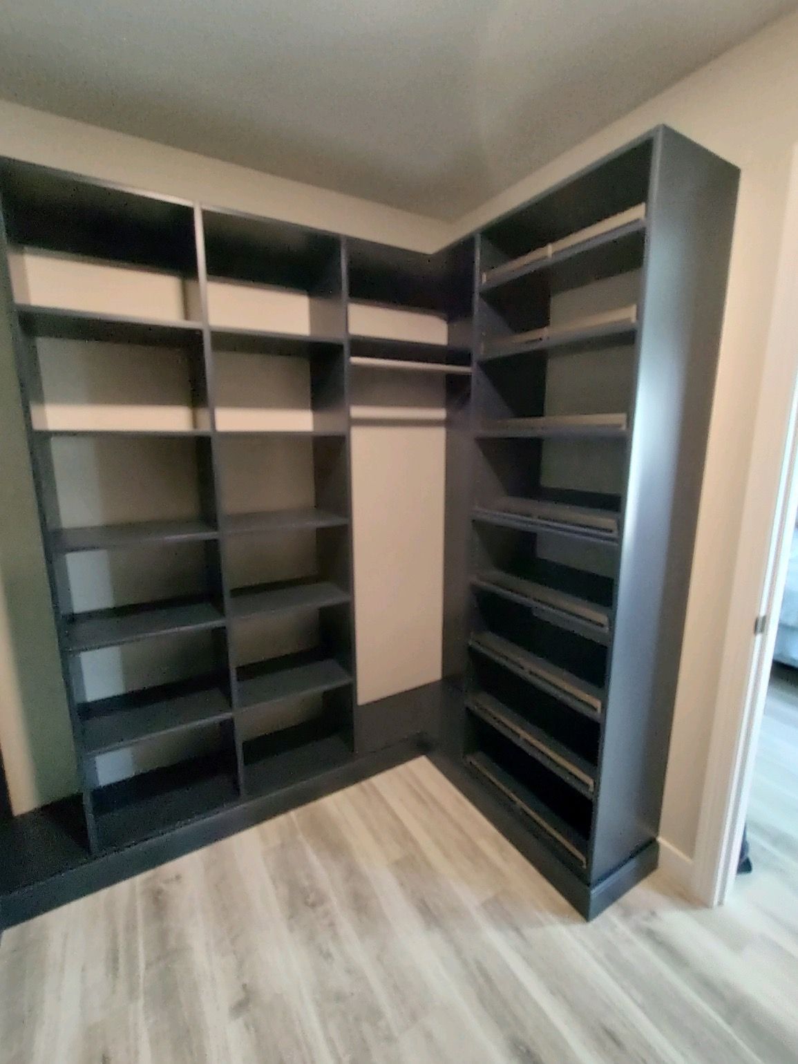 Dark gray corner closet with shelves and hanging rod, on light wood floor.
