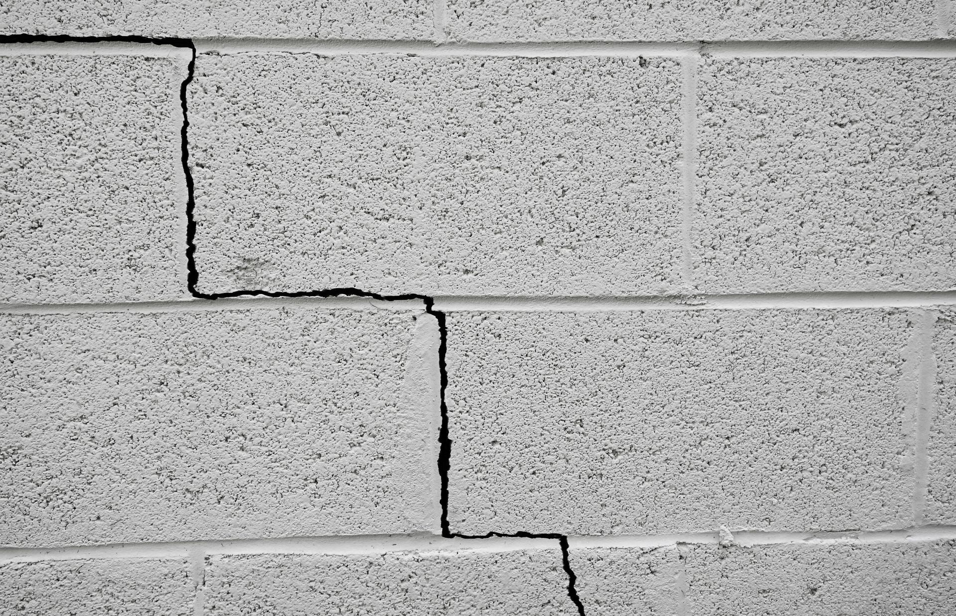 Gray cinder block wall with a large, jagged crack running through several blocks.