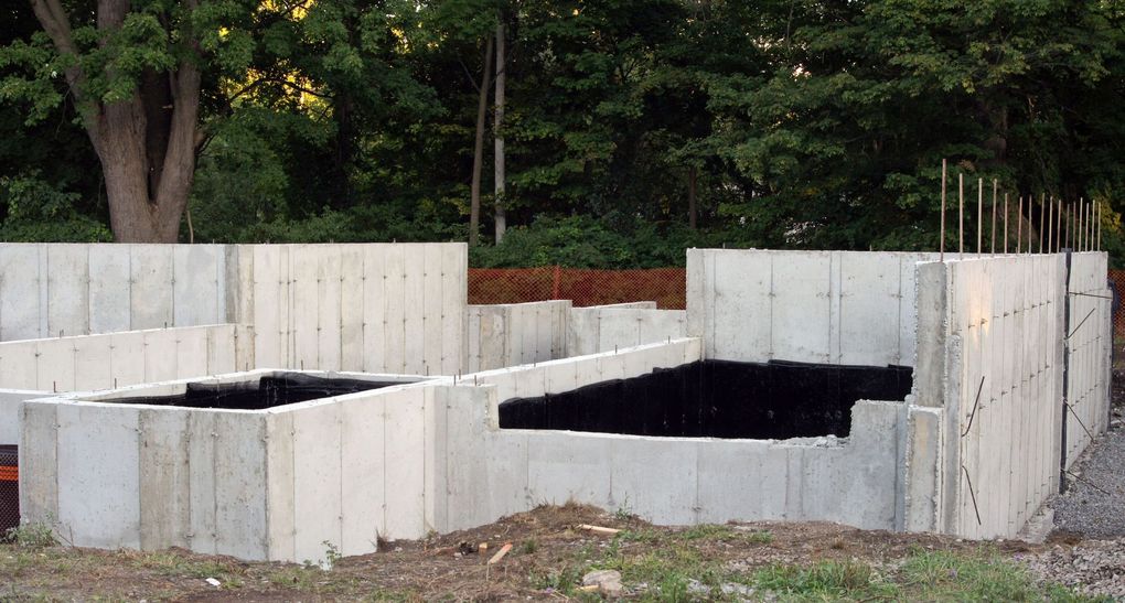 Concrete foundation walls of a building under construction, set in a dirt lot.