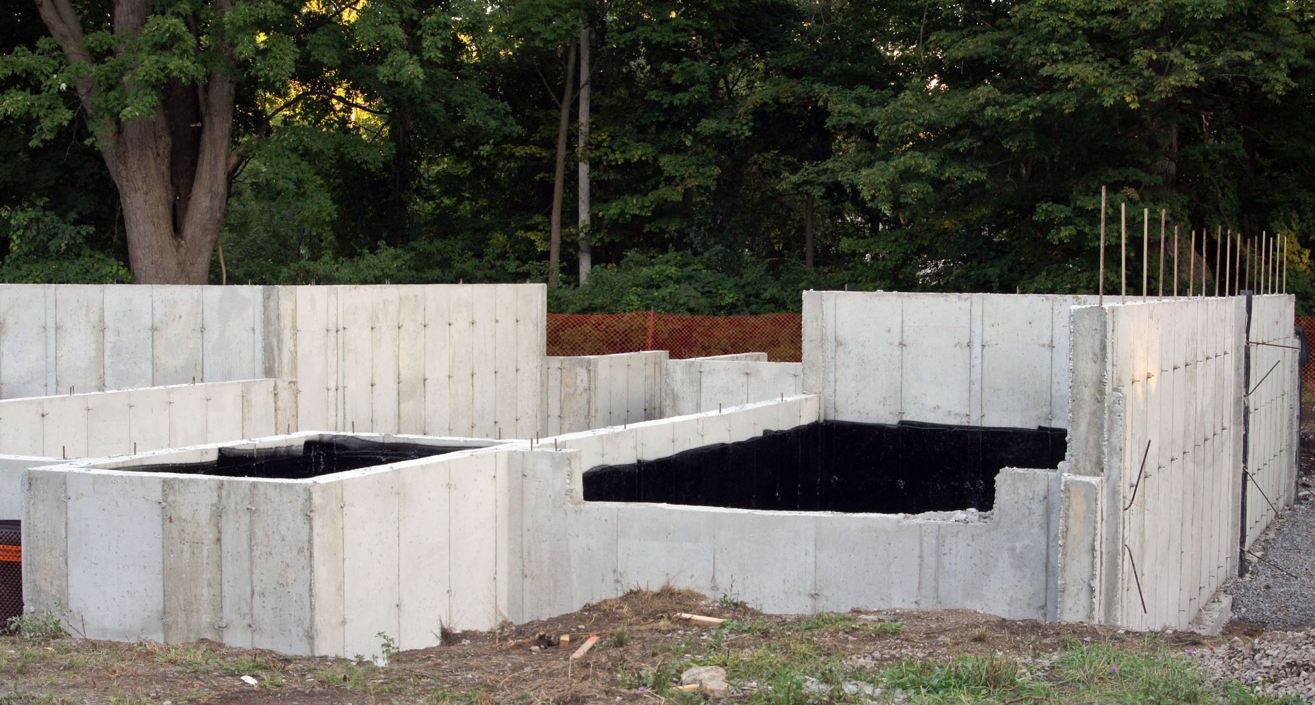 Concrete foundation walls of a building under construction, set in a dirt lot.