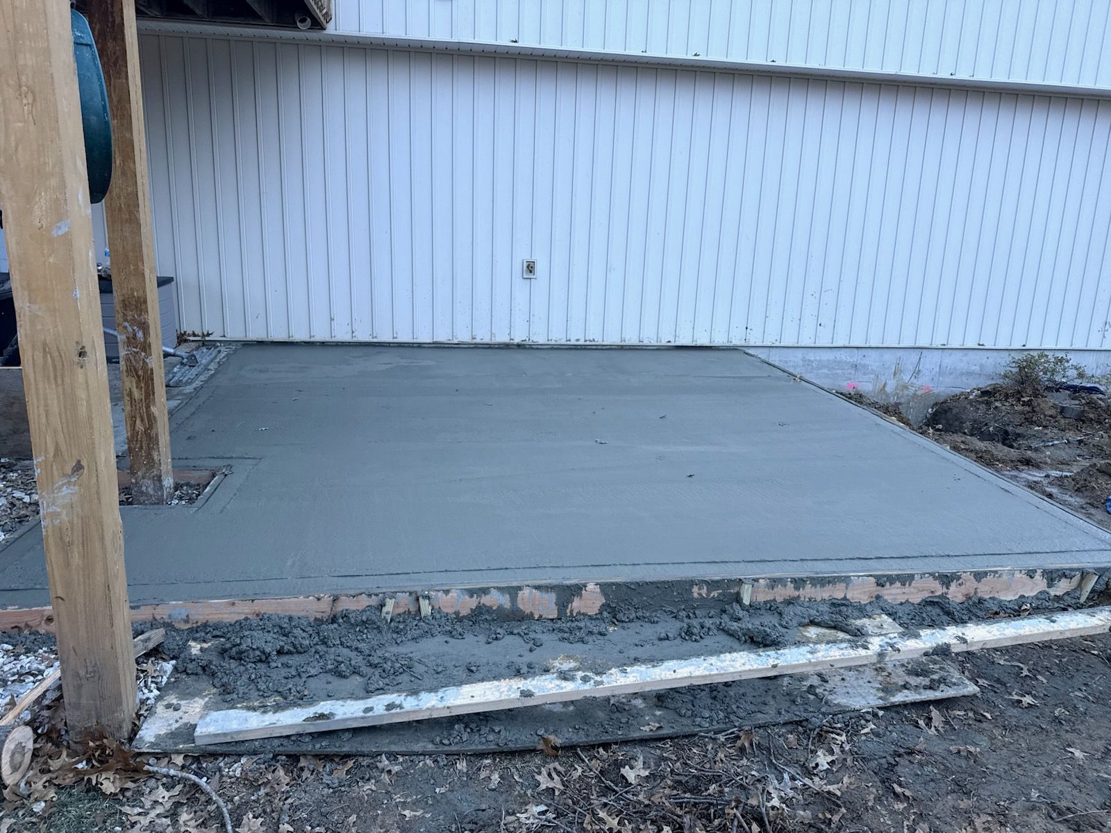 Freshly poured gray concrete patio next to a white building. Construction debris visible.
