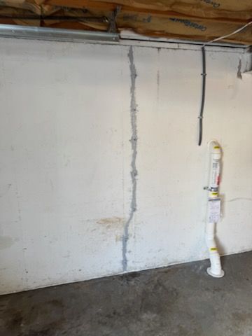 Concrete wall with a vertical crack filled with sealant; drainage pipe.