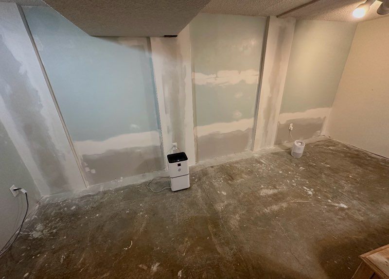 Room under construction: drywall installed on walls, bare concrete floor, paint bucket.