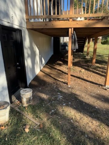 View under a wooden deck with dirt ground, door, and exterior wall.