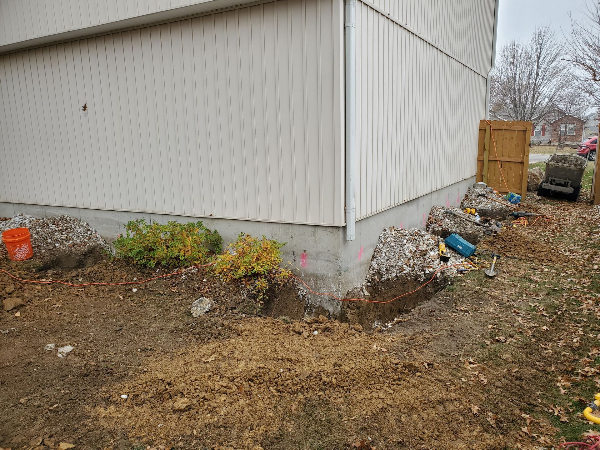 Construction site next to a white building; dirt, leaves, and blue pipes.