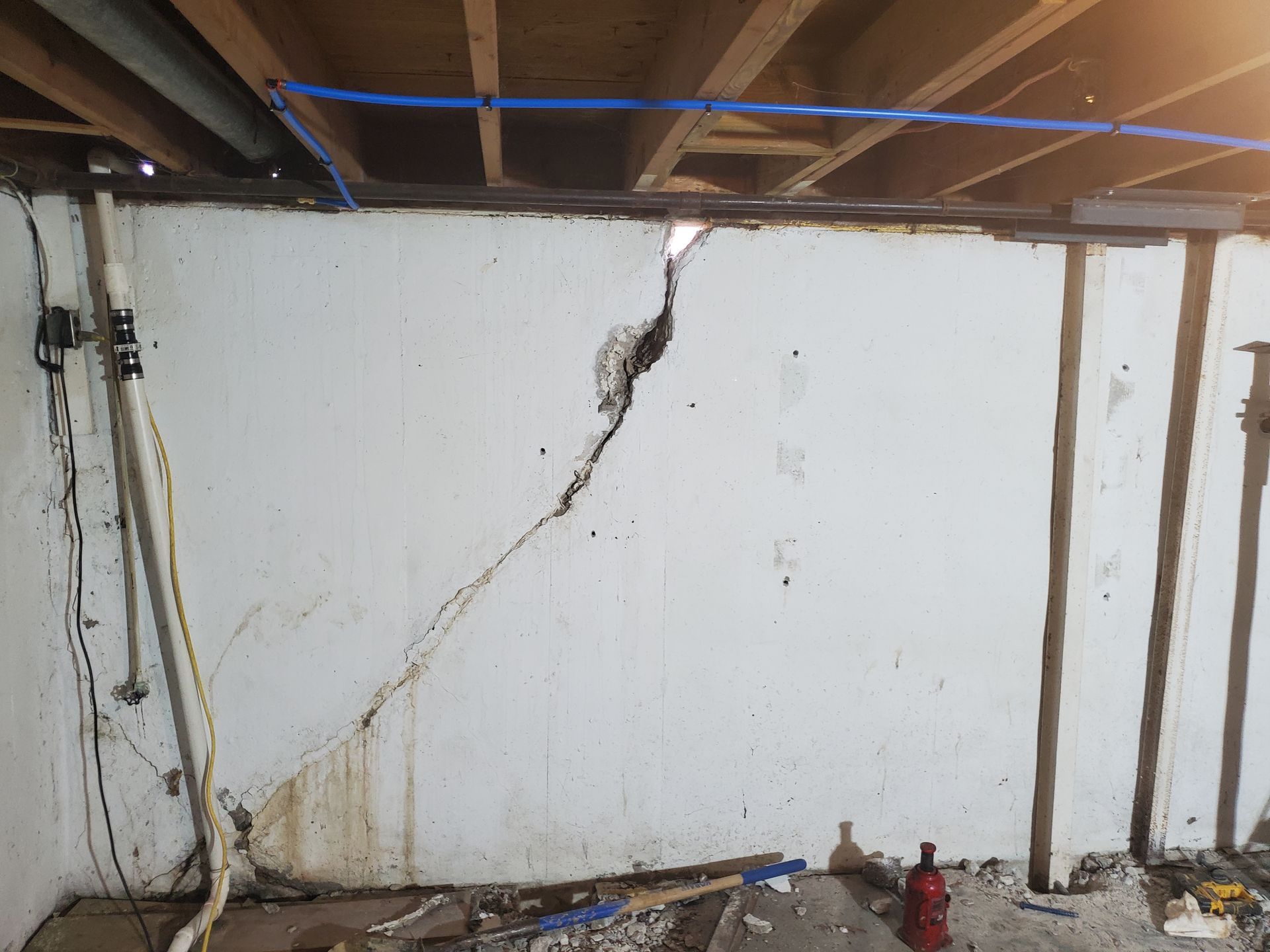 Cracked white basement wall with a large diagonal crack. Water stains and exposed studs visible.