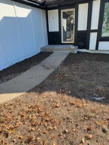 Concrete walkway leading to a front door with a small porch, flanked by newly tilled soil.