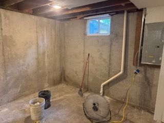 Concrete basement interior with a window, pipes, and buckets.