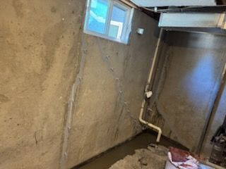 Basement interior with concrete walls, small window, plumbing, and standing water.