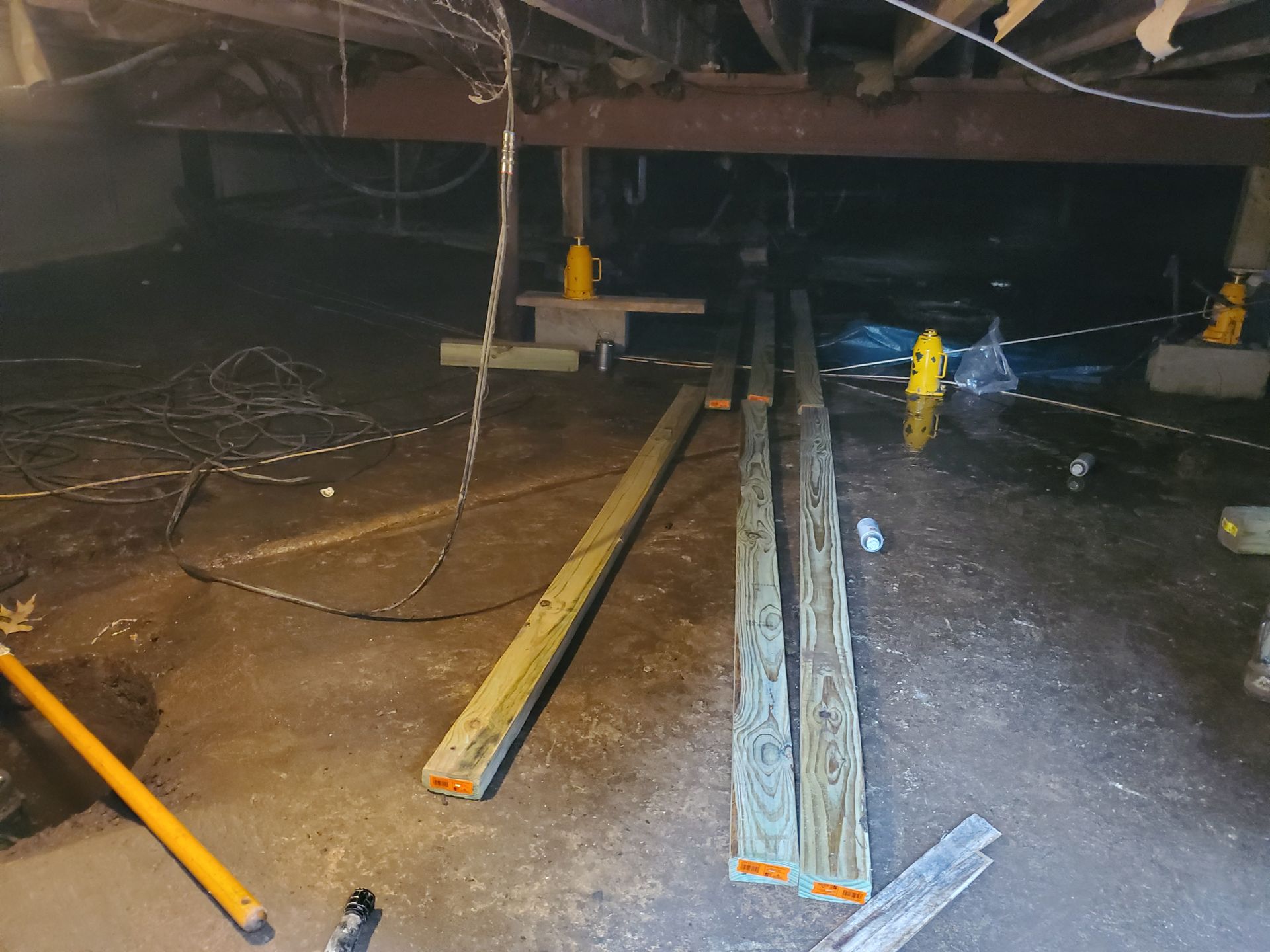 Under-house shot with wooden beams, jack stands, and standing water.