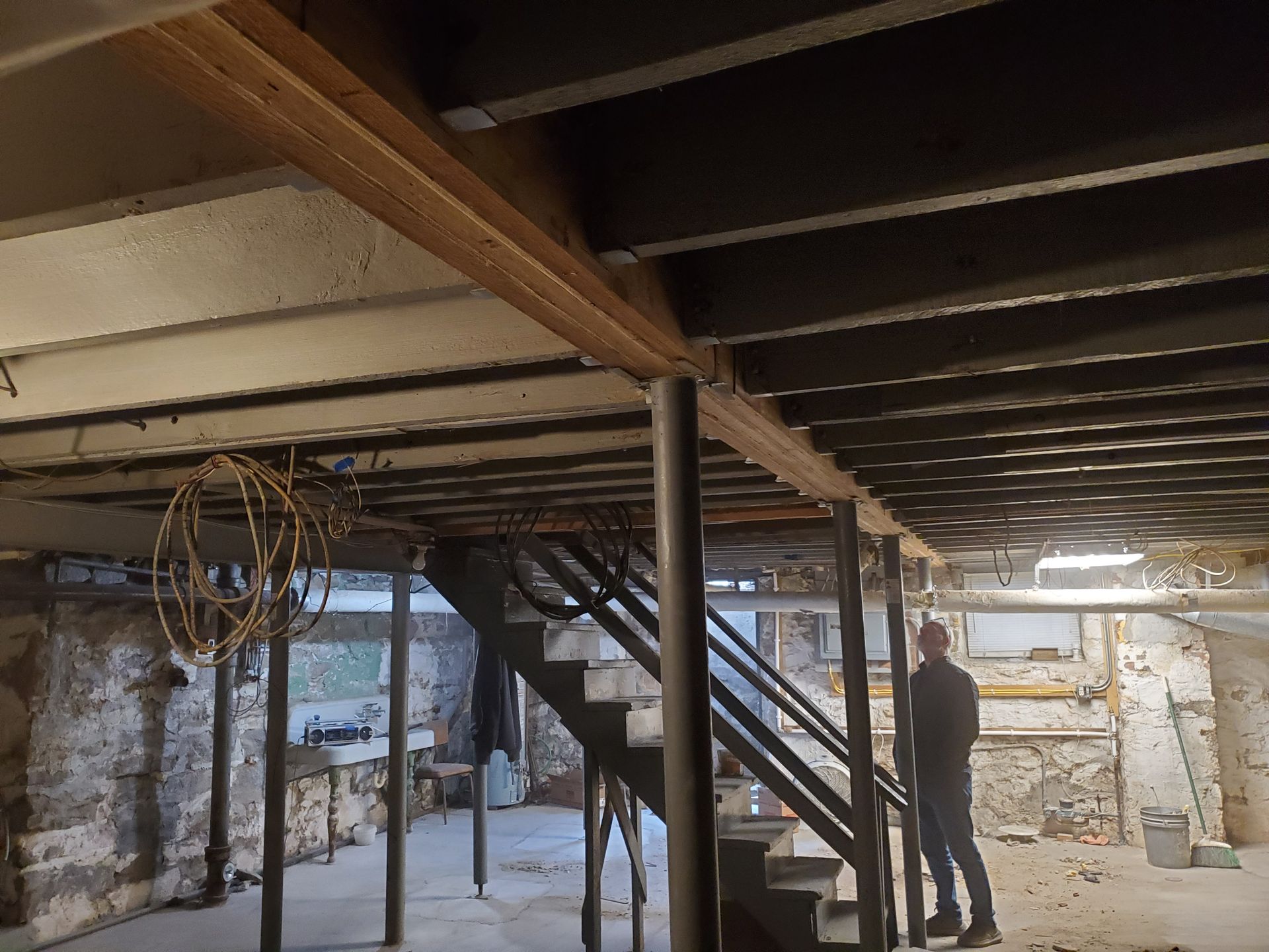 Basement renovation with exposed beams, stairs, and person looking up.