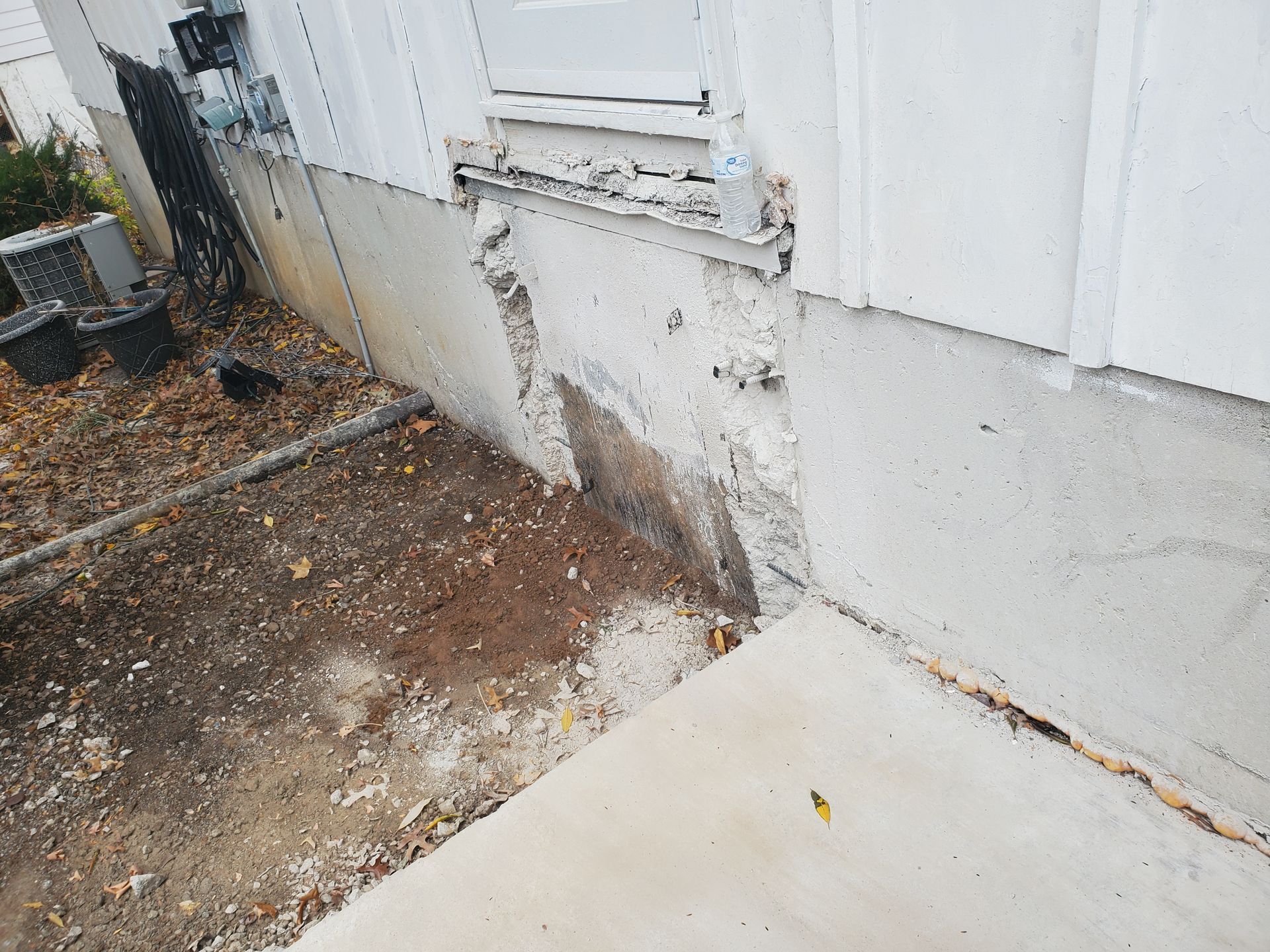 Damaged exterior wall near a window. Concrete foundation is crumbling.