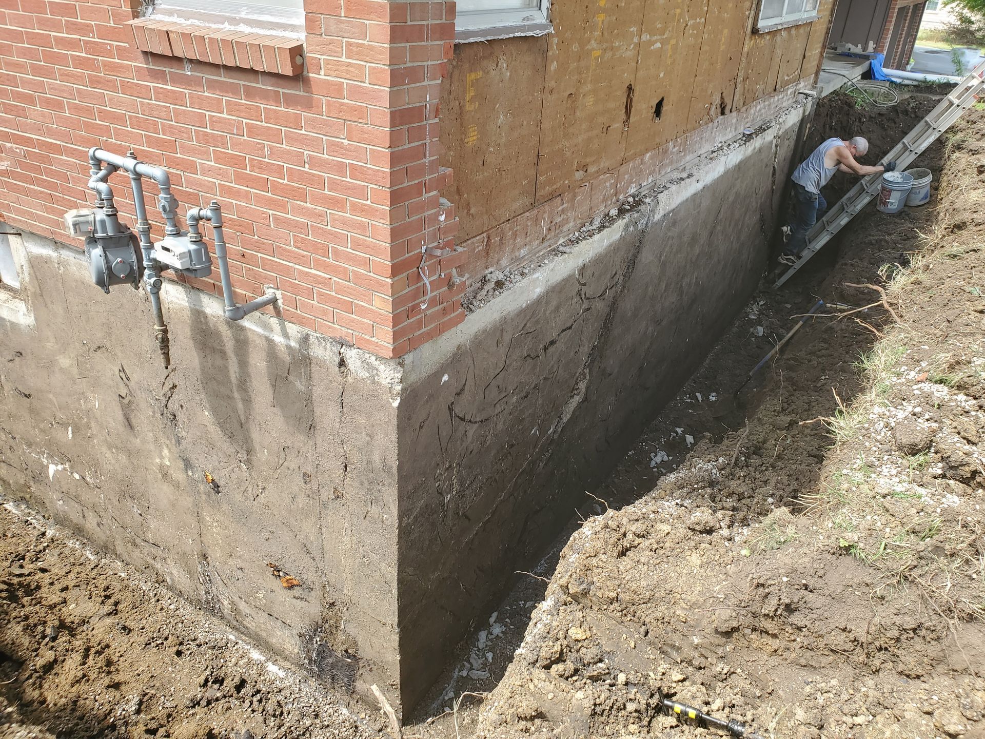 Exterior view of a house foundation being worked on. A person works in a trench.