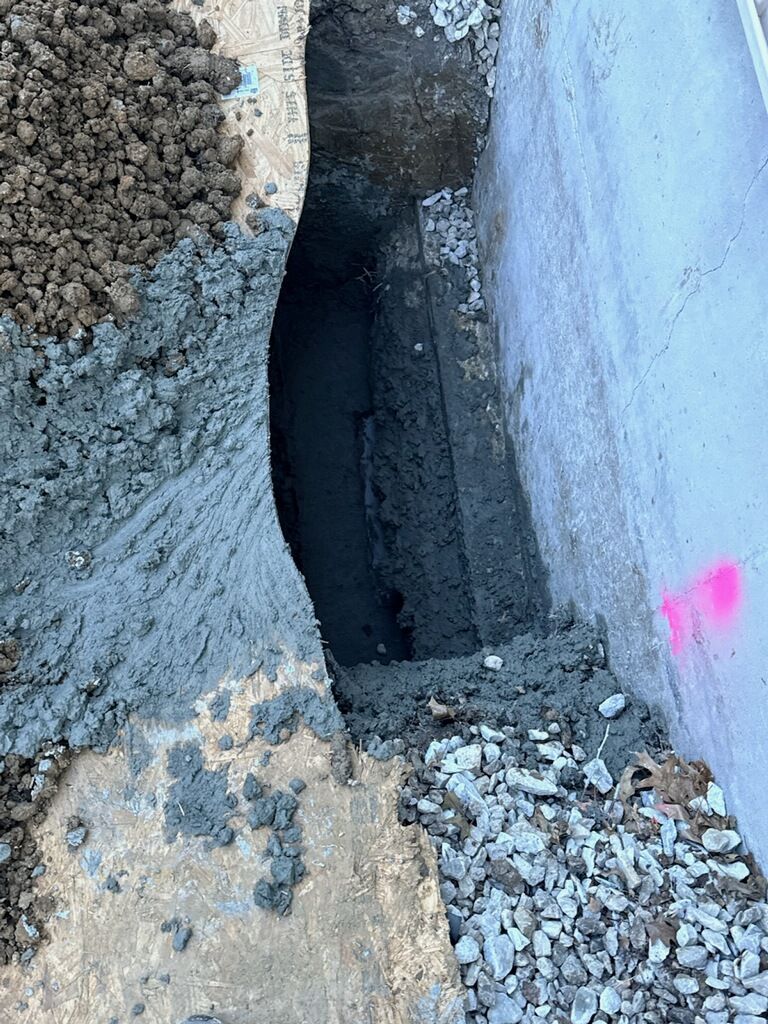 Narrow trench filled with wet cement between a concrete wall and a paved surface.