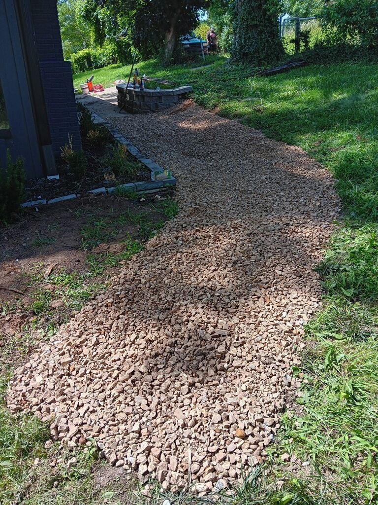 Gravel pathway curving through a grassy yard, leading towards a dark building.