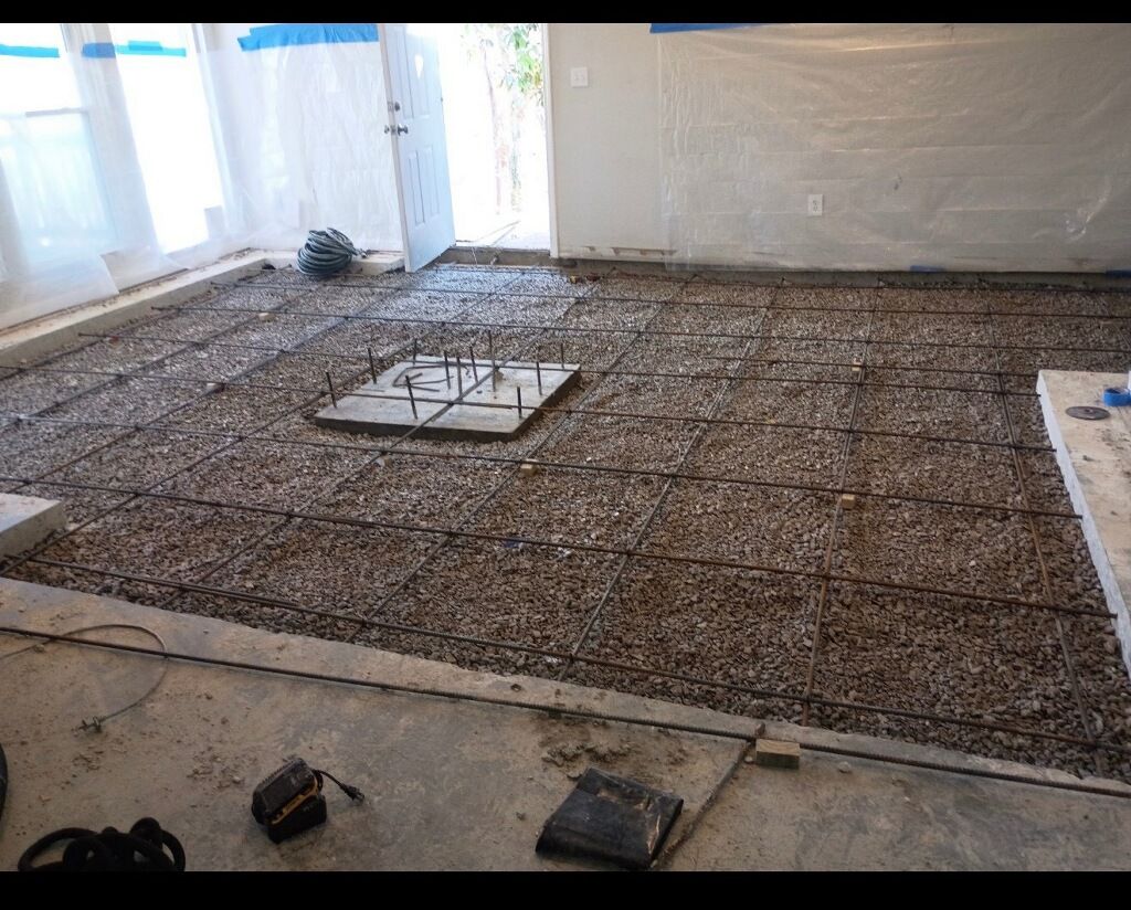 Construction site with exposed aggregate, rebar, and concrete forms on a floor.