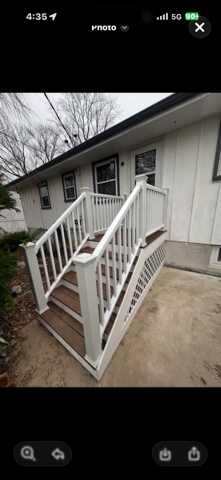 White house with wooden steps and railing leading to the front door. Grey concrete surrounding.
