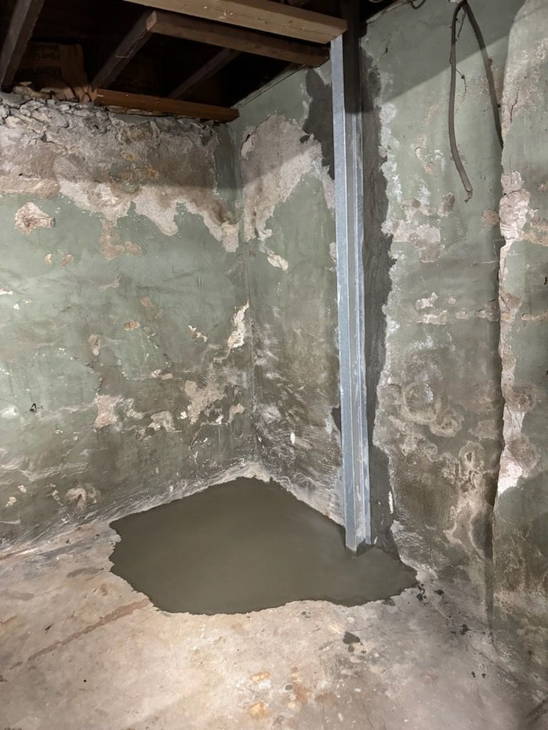 Basement with water pooling on the floor, metal support beam on the wall. Green and grey walls.