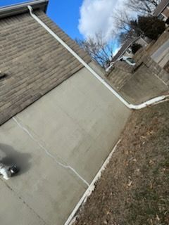 Exterior wall with a white gutter, cracked concrete, and brown brick under a blue sky.