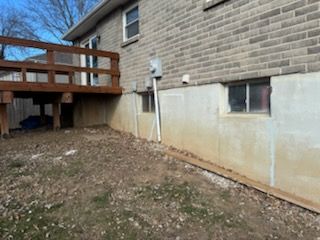 Exterior view of a brick house with a wooden deck and a concrete foundation with windows.  The ground has dry leaves.