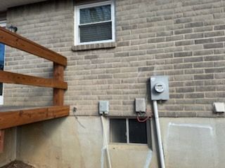 Brick building exterior with a window, deck, electrical boxes, and meter.